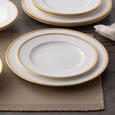 four white and gold plates sitting on top of a brown place mat next to a wooden table