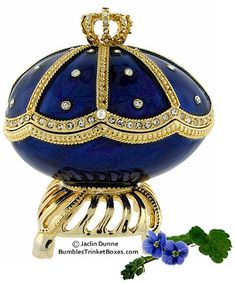 a blue and gold egg with jewels on it's head, sitting next to a purple flower