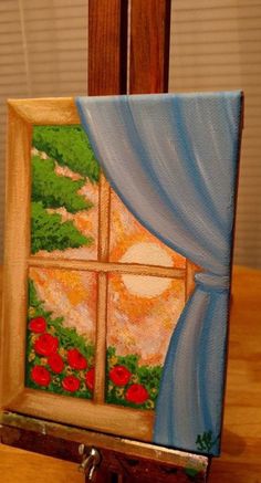 an easel with a painting on it sitting on a wooden table next to a window