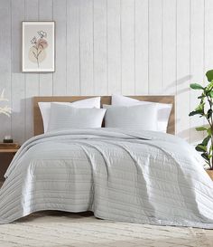 a bed with white sheets and pillows in a room next to a potted plant