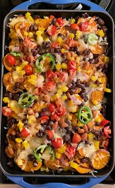 a blue casserole dish filled with black beans, corn, tomatoes and cheese