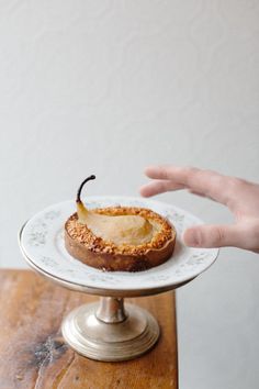 a person is reaching for a piece of food on a cake plate that has been placed on top of a wooden table