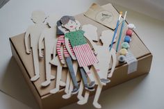 an open box with paper cutouts of people and sewing supplies in it on top of a table