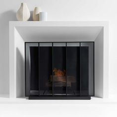 a white fireplace with black glass doors and a vase on top