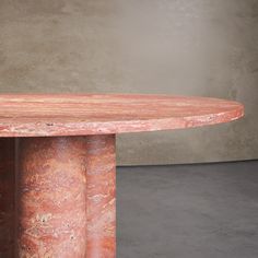 a red marble table sitting on top of a cement floor next to a gray wall