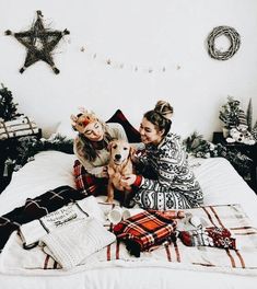 two women are sitting on a bed with their dog and christmas decorations around the room