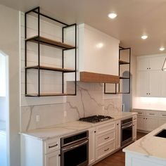 an empty kitchen with white cabinets and marble counter tops, along with open shelving