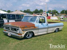 an old pickup truck parked in the grass at a car show with other trucks behind it