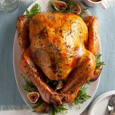 a roasted turkey with figs and herbs on a white plate next to silverware