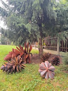 two large metal flowers sitting in the grass next to a pine cone tree and fence