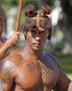 a man with tattoos on his body holding a stick and wearing a headdress