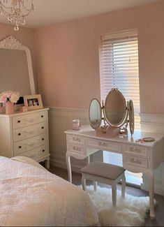 a bedroom with pink walls, white furniture and a chandelier hanging from the ceiling