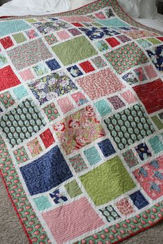 a bed with a colorful quilt on it's cover and white sheets in the background