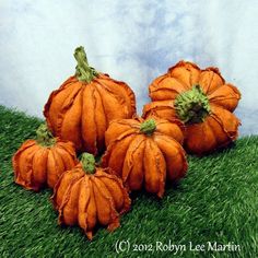 four orange pumpkins sitting in the grass on top of a green field with blue sky behind them