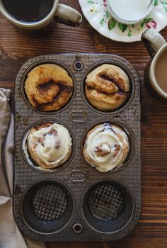 cupcakes with cinnamon rolls in a muffin tin next to two cups of coffee