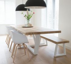 a wooden table with white chairs and two black lamps hanging from it's ceiling