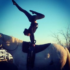 a woman doing a handstand on top of a white horse