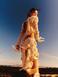 a woman in a white dress walking across a field