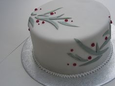 a white cake with red berries and leaves on it sitting on a silver platter