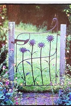 an iron gate with flowers on it in the middle of some grass and plants behind it