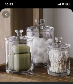 three glass containers filled with candles on top of a wooden table