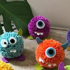 four colorful pom poms sitting on top of a wooden table next to a green leaf