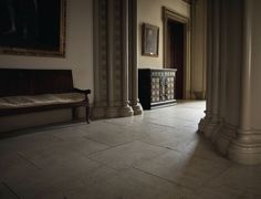 an empty room with columns and a bench in the center, near a painting on the wall