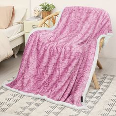 a pink and white blanket sitting on top of a bed next to a wooden chair