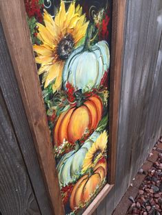 a painting of pumpkins and sunflowers on a door with a fence in the background