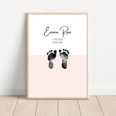 a pink and black print with two baby footprints on it, in front of a white wall