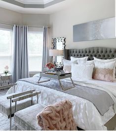 a bedroom with white and gray bedding, pink throw pillows, grey headboard