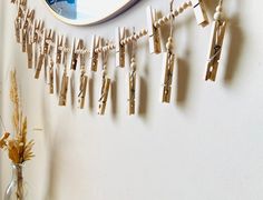 a clock hanging on the side of a wall next to clothes pins and dried flowers