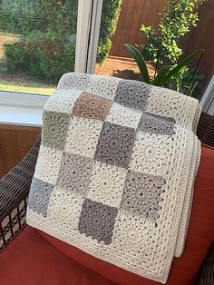 a crocheted blanket sitting on top of a chair next to a potted plant