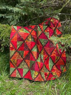 a red and green quilt sitting on top of a grass covered field next to a tree