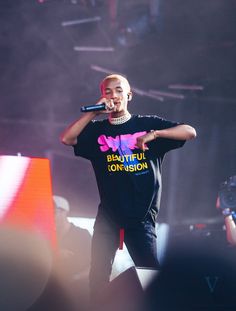 a man standing on top of a stage holding a microphone in his right hand and wearing a black shirt