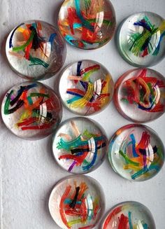 six glass magnets with different colored paint designs on them, all in various shapes and sizes