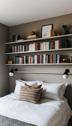 a bed with white sheets and pillows in front of bookshelves on the wall