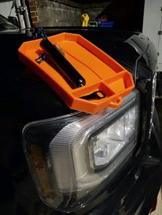 an orange tool box sitting on the hood of a black car with it's headlight turned down