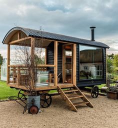 a tiny house on wheels in the middle of a grassy area with stairs leading up to it