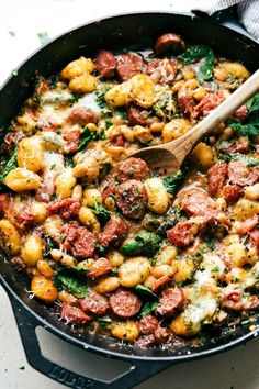 a skillet filled with sausage, spinach and cheese on top of a wooden spoon