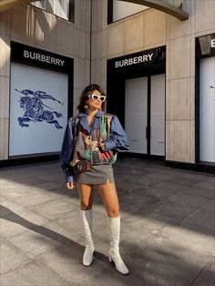 a woman standing in front of a burberry store wearing white boots and a denim jacket