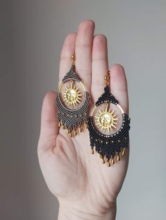 a pair of earrings in the palm of someone's hand, with gold and black details