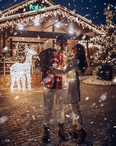 a man and woman standing in front of a building with christmas lights