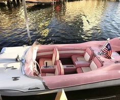 a pink and white boat sitting in the water next to a dock with an american flag on it