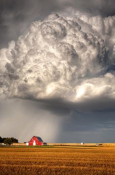 a large cloud looms over a red barn in the middle of an open field