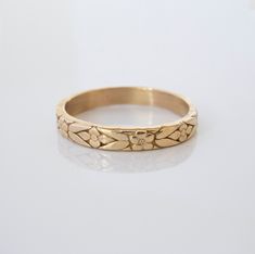 a gold wedding band with flowers on the side and hearts in the middle, sitting on a white surface