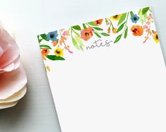 a notepad sitting on top of a table next to a pink flower