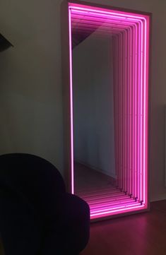 a large pink mirror sitting on top of a wooden floor next to a black chair