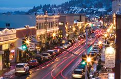 a city street filled with lots of traffic next to tall buildings and snow covered mountains