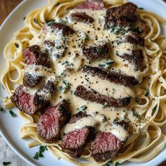 a white plate topped with pasta and steak covered in gravy on top of a wooden table